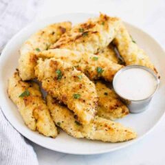 Crispy baked chicken tenders on a white plate with dipping sauce.