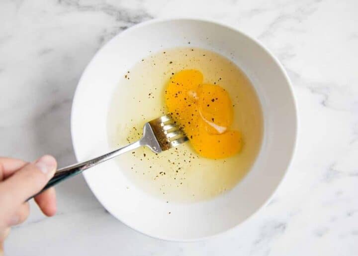 whisking eggs in a white bowl with a fork 
