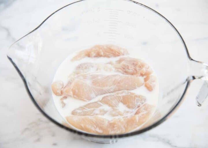 chicken tenders soaking in buttermilk in glass bowl