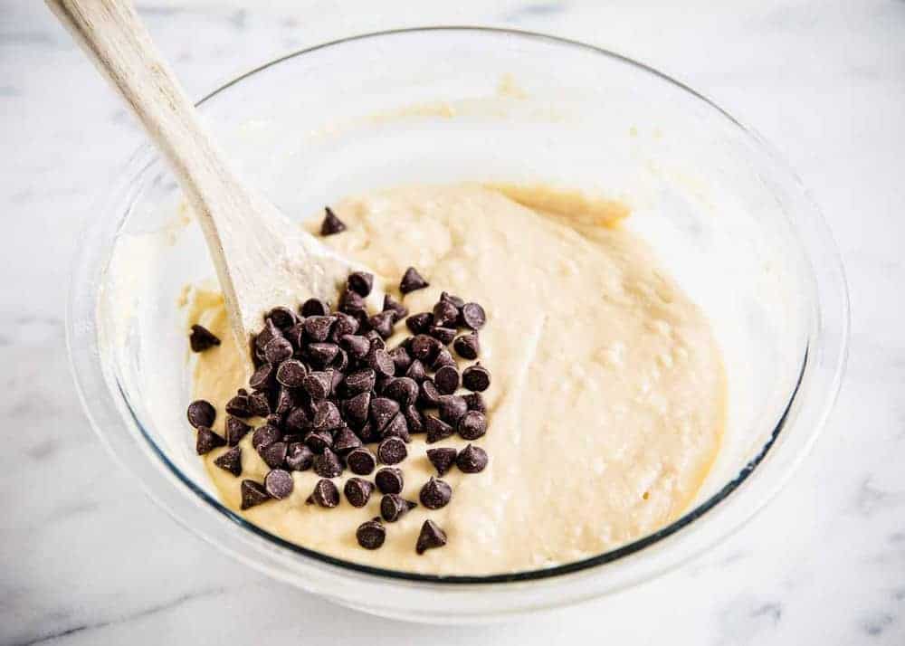 folding chocolate chips into bowl of chocolate chip pancake batter with a wooden spoon 