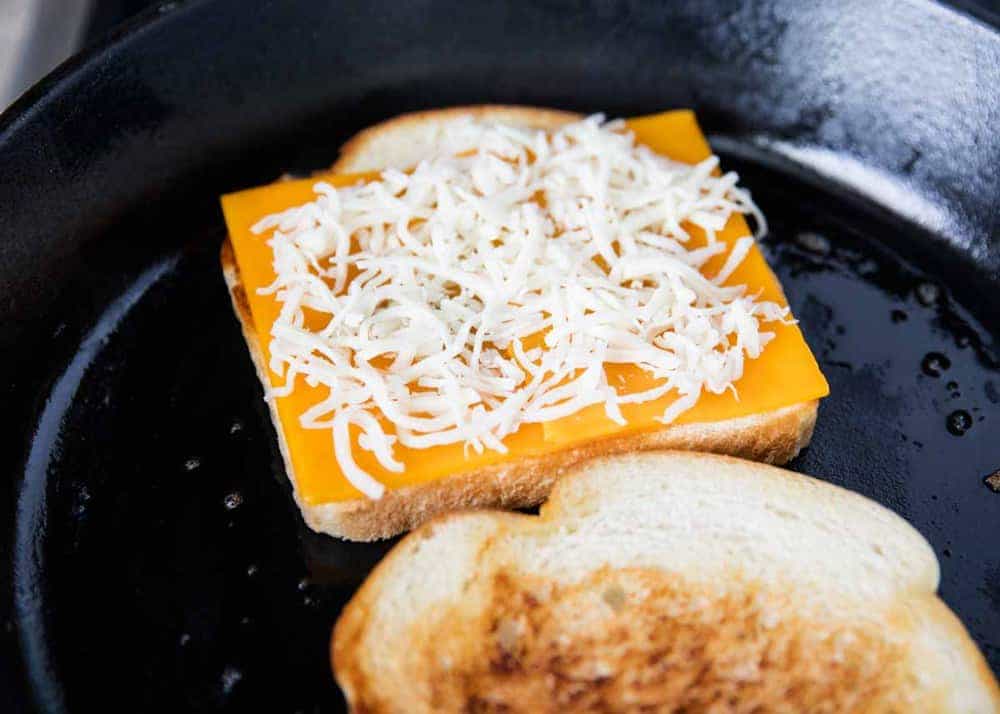 Adding cheese on top of toasted bread in a skillet.