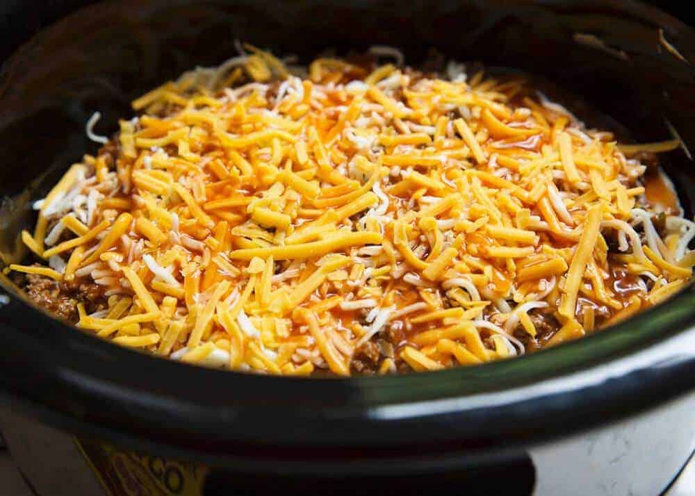 Taco lasagna in the slow cooker topped with shredded cheese.