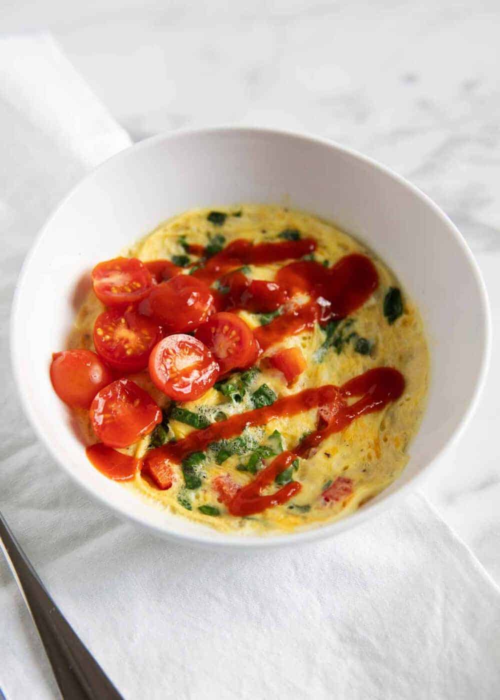 Bowl of microwave eggs topped with sliced tomatoes and ketchup.