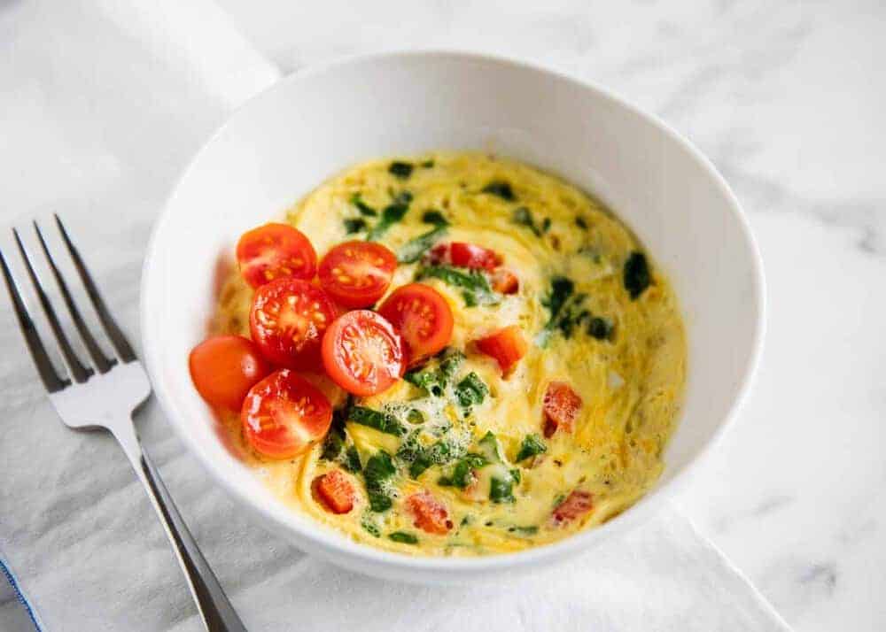 Microwave scrambled eggs in a white bowl with diced tomatoes on top.