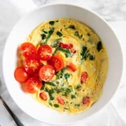 scrambled eggs in a white bowl with fresh chopped baby tomatoes