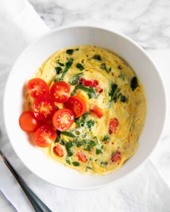 scrambled eggs in a white bowl with fresh chopped baby tomatoes