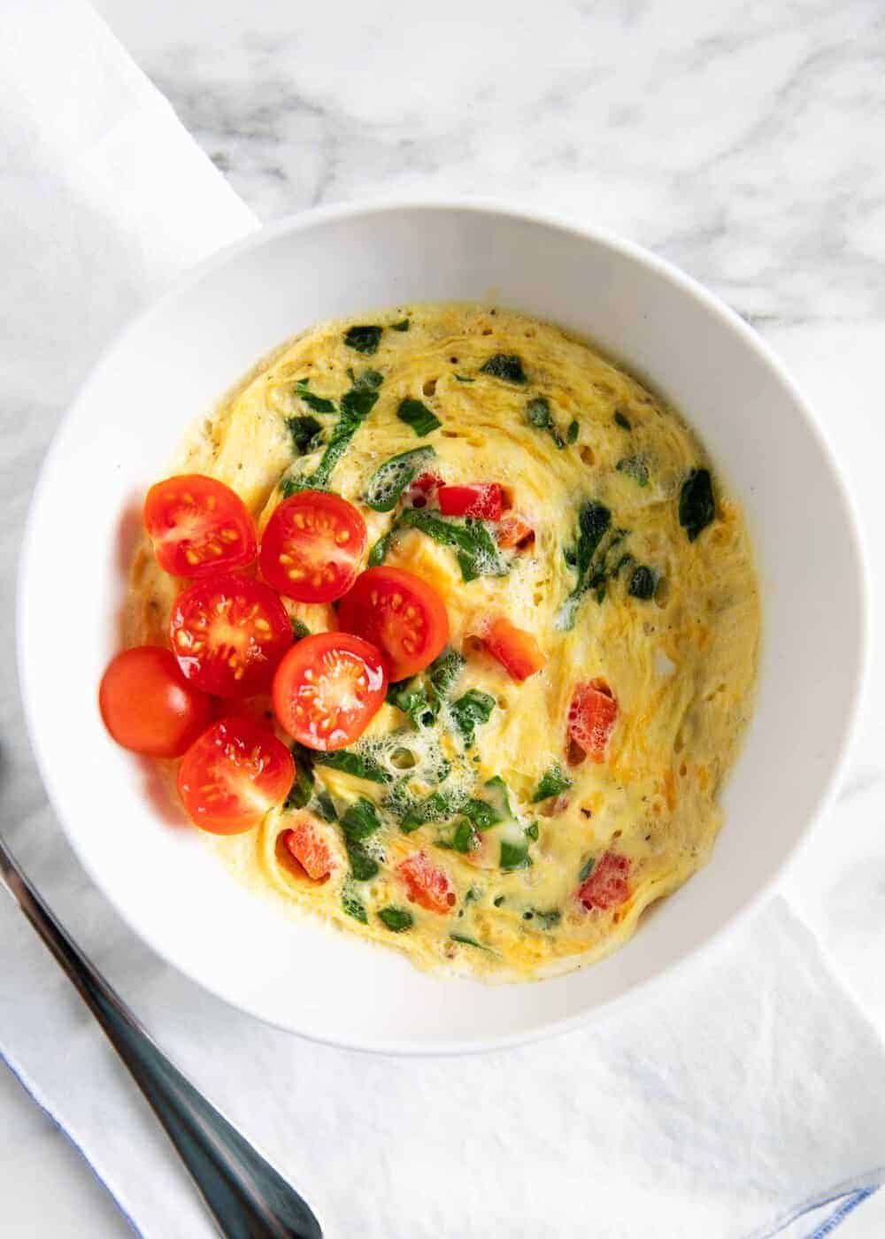 Scrambled eggs in a white bowl with fresh chopped baby tomatoes.