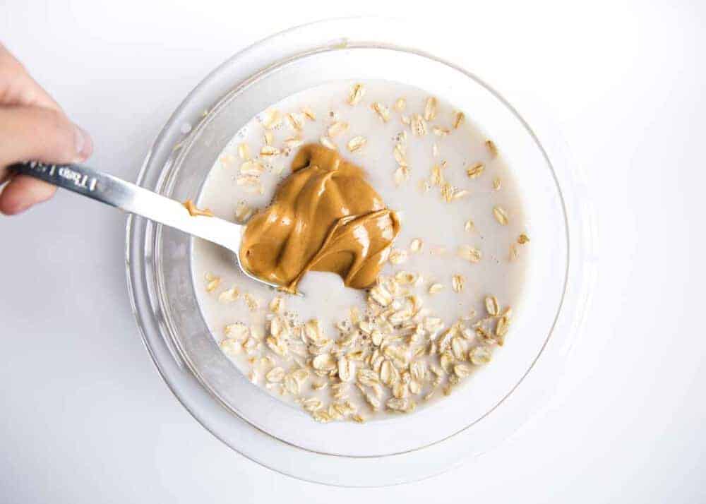 Mixing together peanut butter, oats and almond milk in a glass bowl.