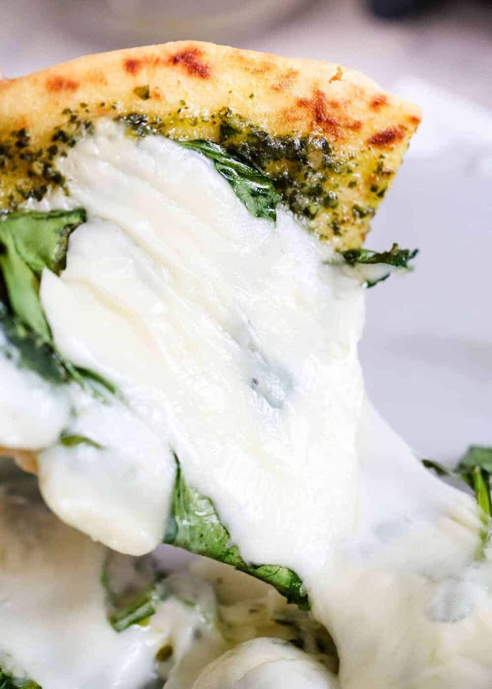 Slice of pesto pizza with melted cheese.