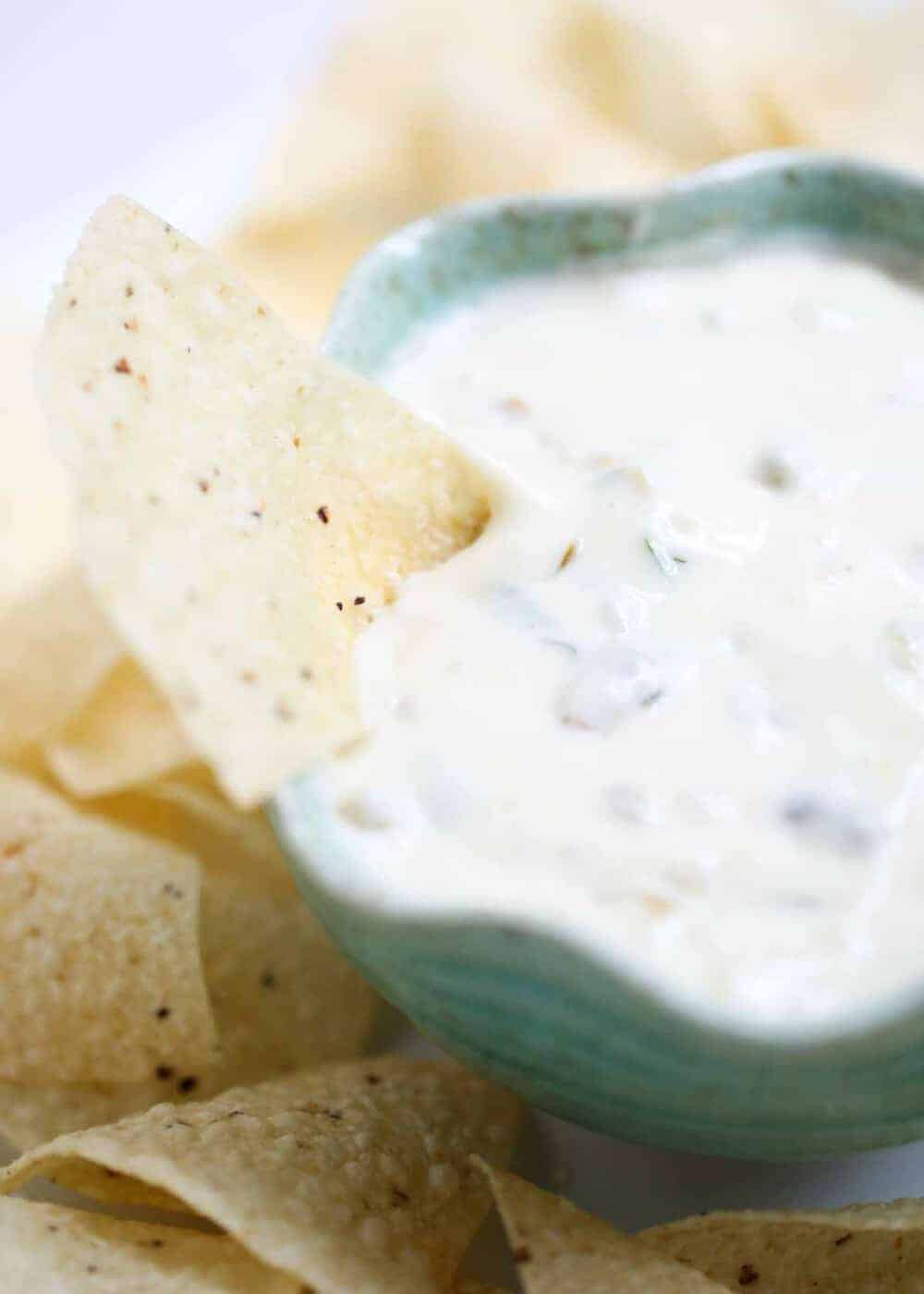 Dipping a chip in bowl of white queso dip.