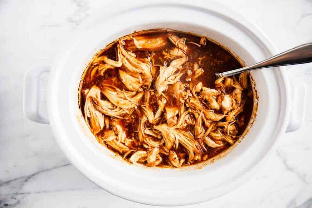 BBQ pulled chicken in a white crockpot with a fork.