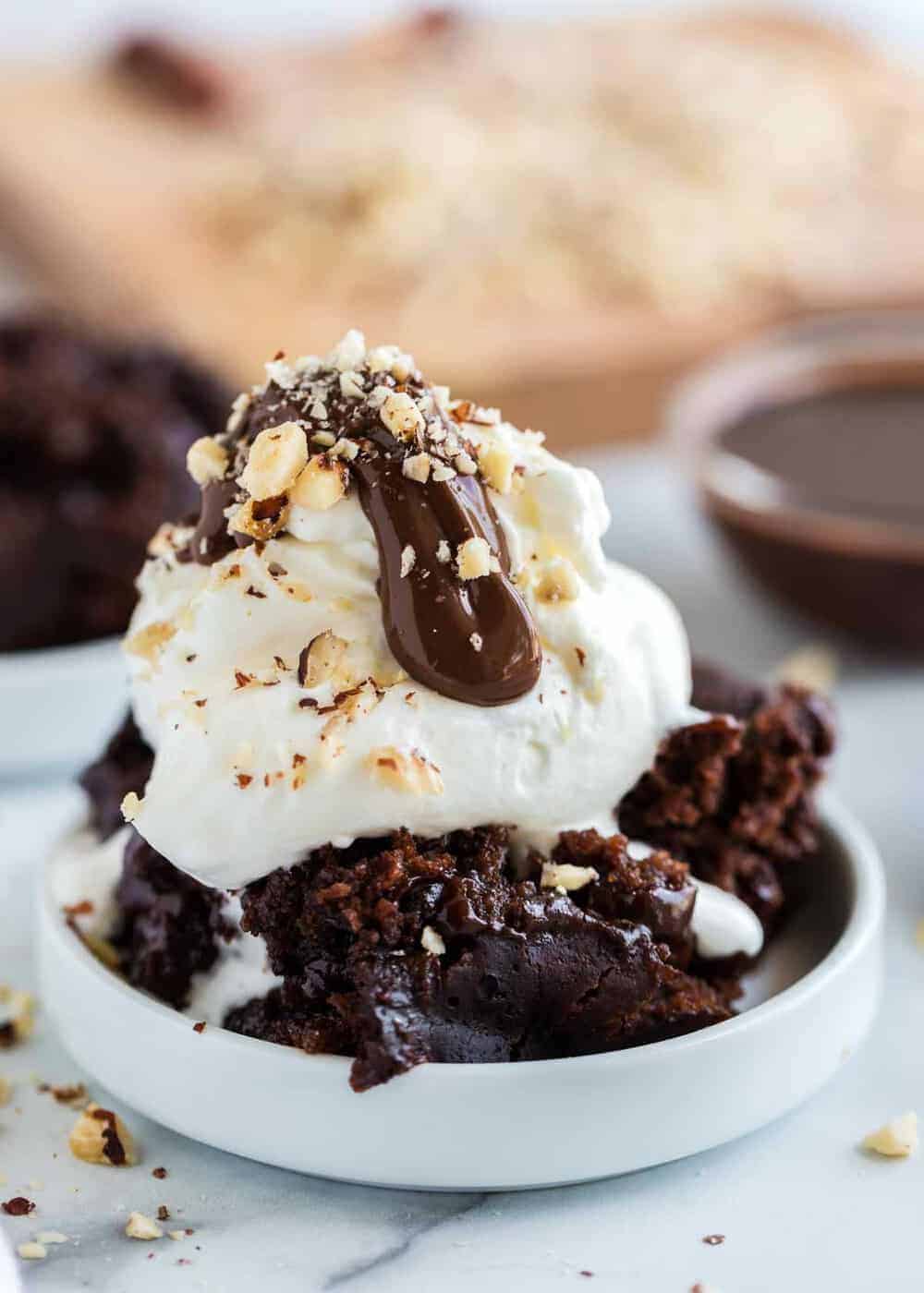 Bowl of crockpot chocolate cake topped with ice cream, nuts and hot fudge.