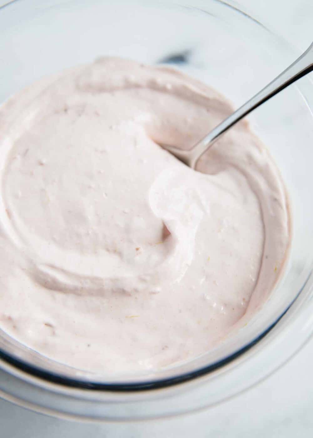 Strawberry fruit dip ingredients mixed together in a bowl with a silver spoon. 