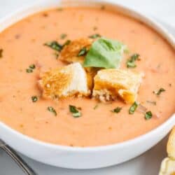 bowl of tomato soup with grilled cheese croutons and fresh basil on top