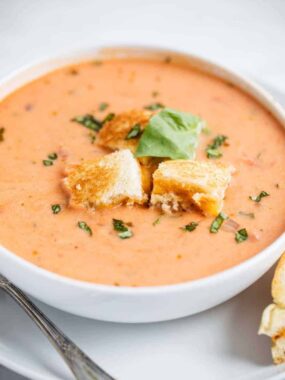 bowl of tomato soup with grilled cheese croutons and fresh basil on top