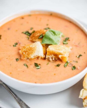 bowl of tomato soup with grilled cheese croutons and fresh basil on top
