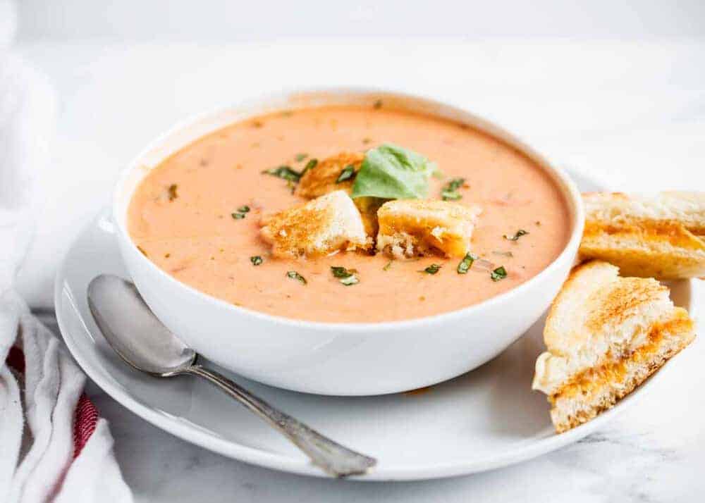bowl of creamy tomato soup served with a grilled cheese and fresh basil