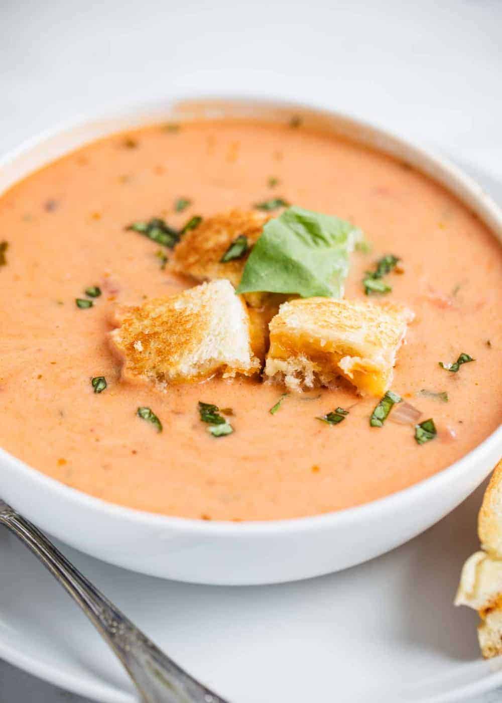 bowl of tomato soup with grilled cheese croutons and fresh basil on top 