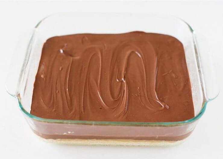 spreading chocolate layer on top of twix cookie bars in baking dish