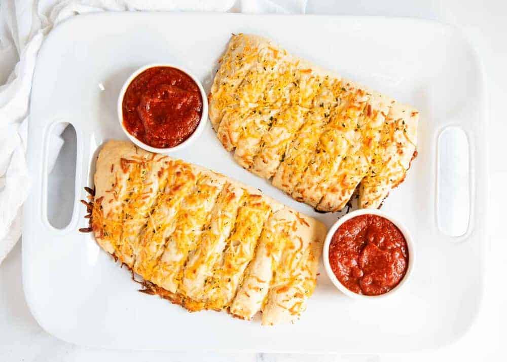 Cheesy Garlic Bread - Delicious homemade bread stuffed with layers of gooey cheese and garlic. Pure cheesy goodness, inside and out! Cheesy garlic bread on a white serving tray with marinara sauce.