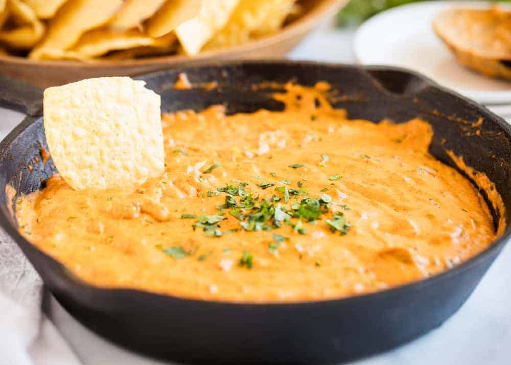 Dipping a chip into chili cheese dip in a cast iron skillet.