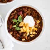 bowl of homemade chili topped with sour cream, cheese, cilantro and crushed chips