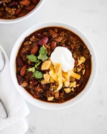 bowl of homemade chili topped with sour cream, cheese, cilantro and crushed chips