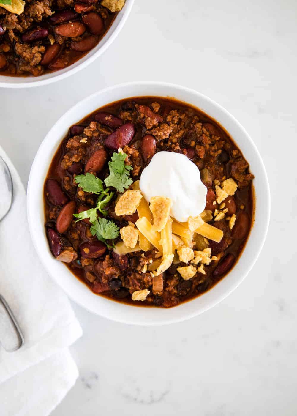 bowl of chili with shredded cheese, sour cream and cilantro 