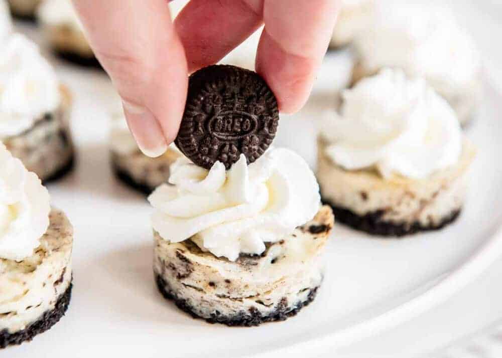 Adding a mini Oreo on top of a mini Oreo cheesecake.