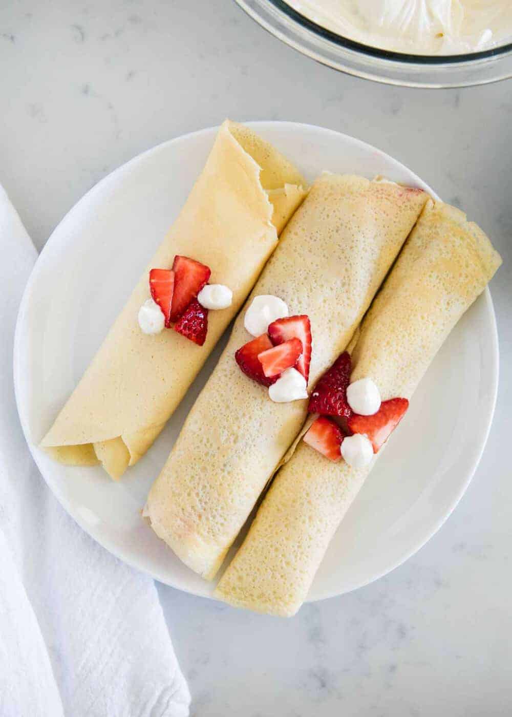 plate of rolled crepes topped with cream cheese filling and strawberries 