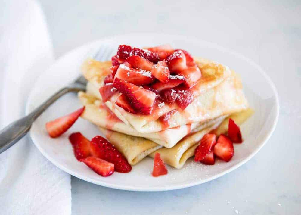 Plate of crepes with strawberry crepe filling on top.