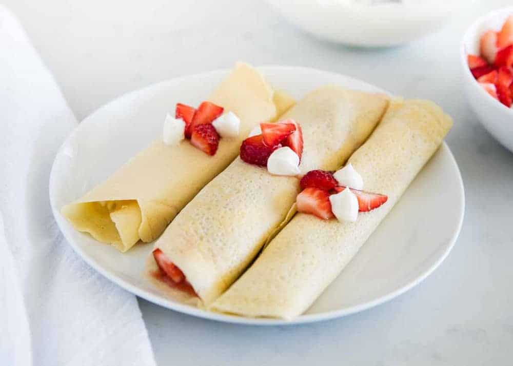 plate full of crepes with cream cheese crepe filling and chopped strawberries 