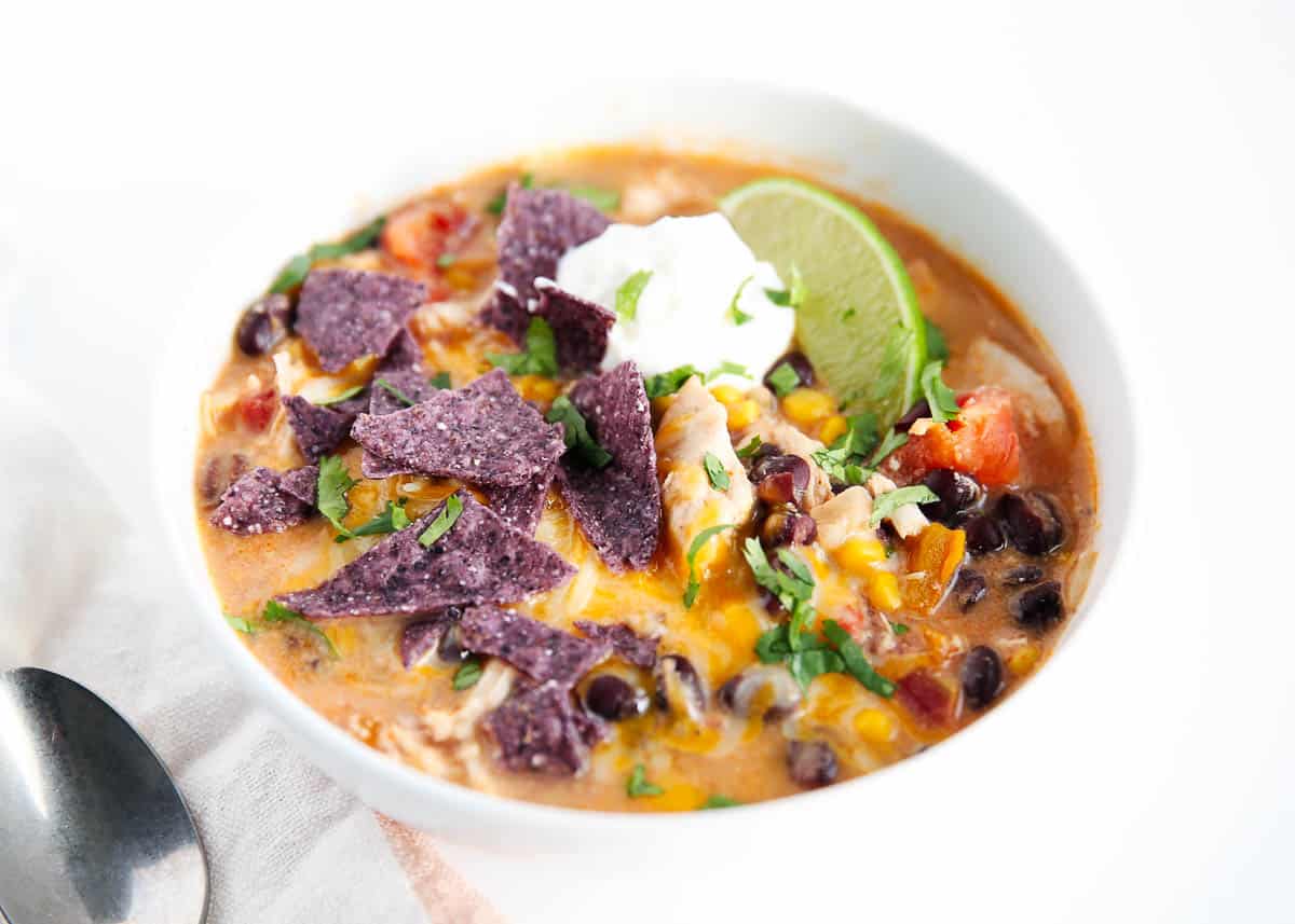 Chicken enchilada soup in white bowl with toppings.