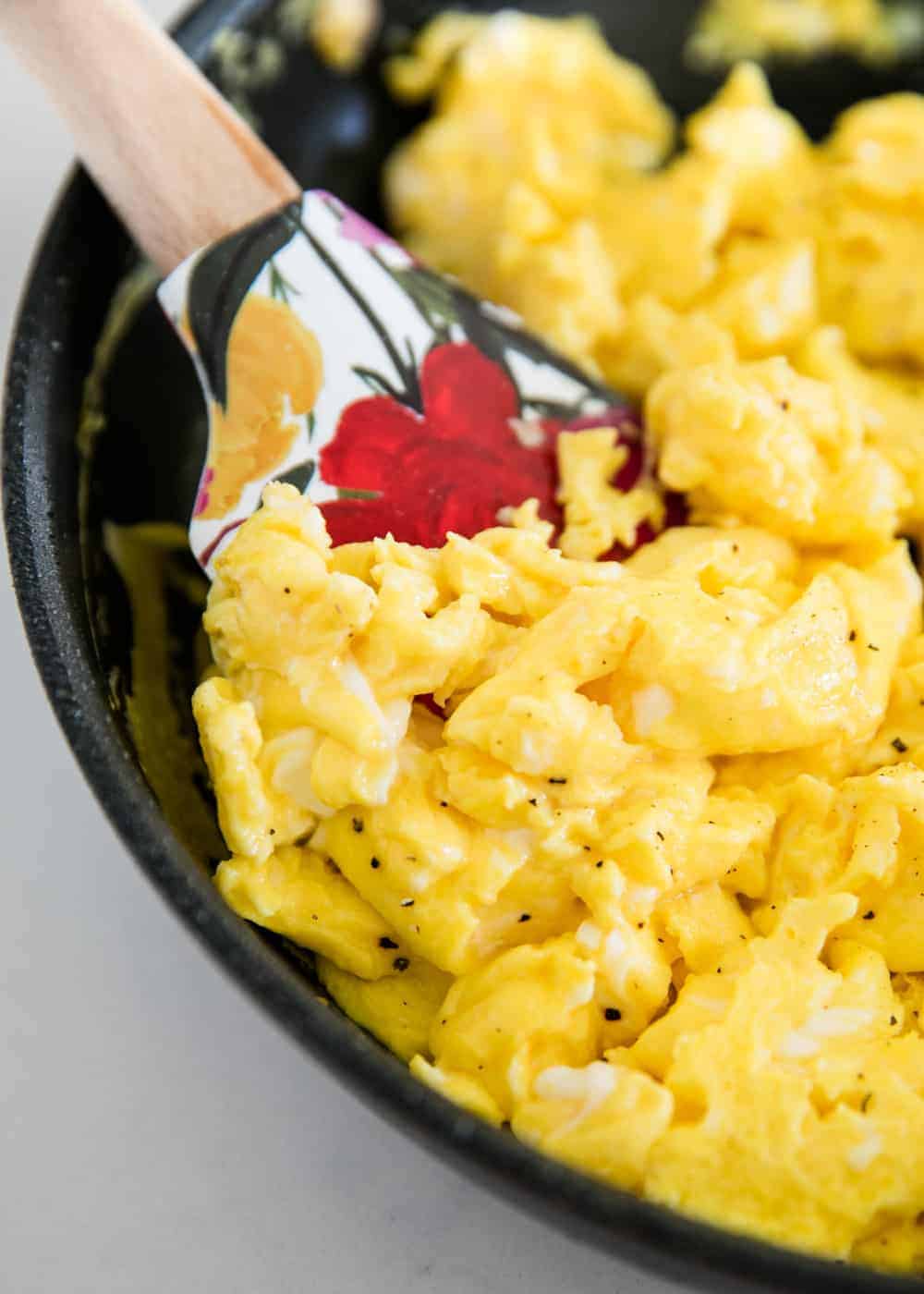 Fluffy scrambled eggs in skillet with colorful spatula.
