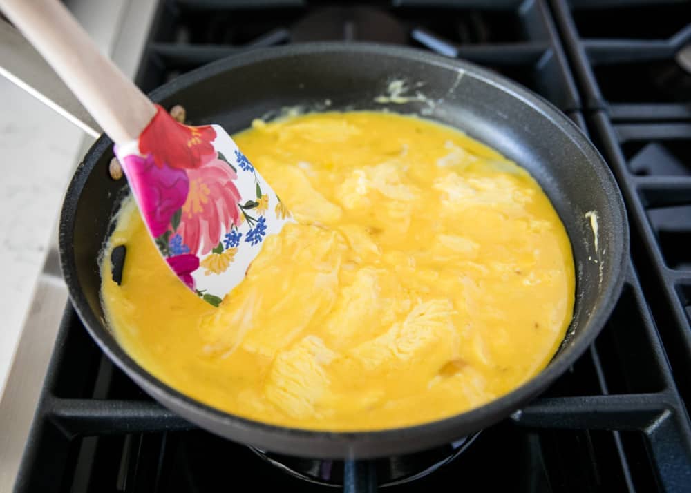 Scrambling eggs in skillet with a colorful spatula.