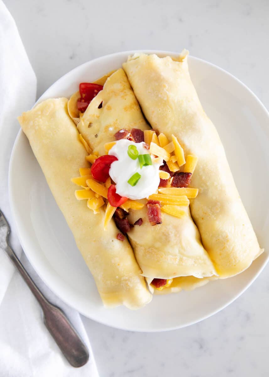 Learn how to make savory crepes in the blender in a matter of minutes! Then add your favorite fillings like scrambled eggs, bacon and cheese for the ultimate breakfast idea. Savory crepes on a plate.