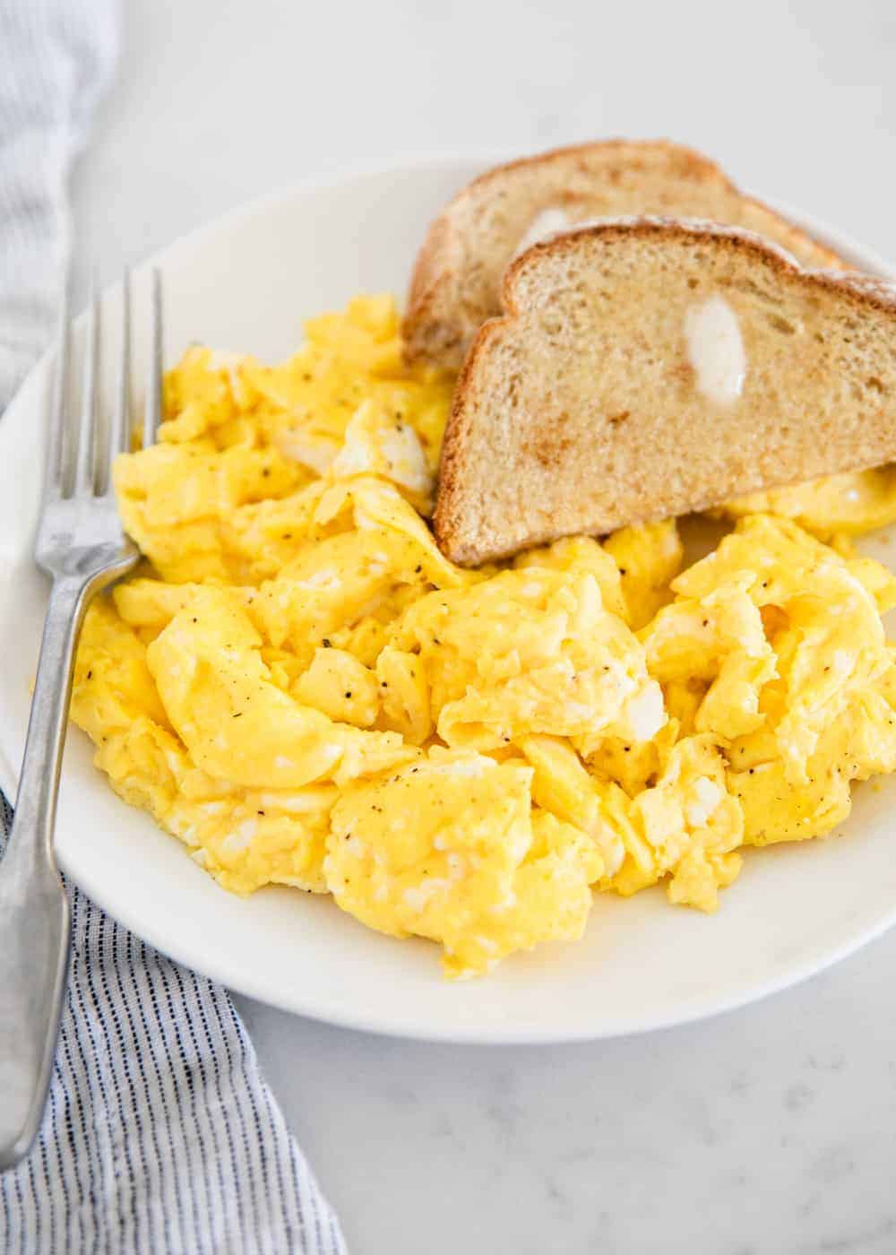 Scrambled eggs on white plate with toast.