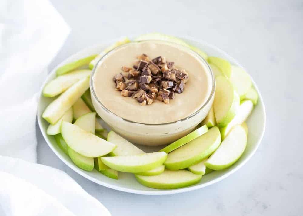Sliced apples and a bowl of caramel dip topped with toffee bits.