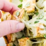 pulling out a piece of cheesy pesto bread with finger
