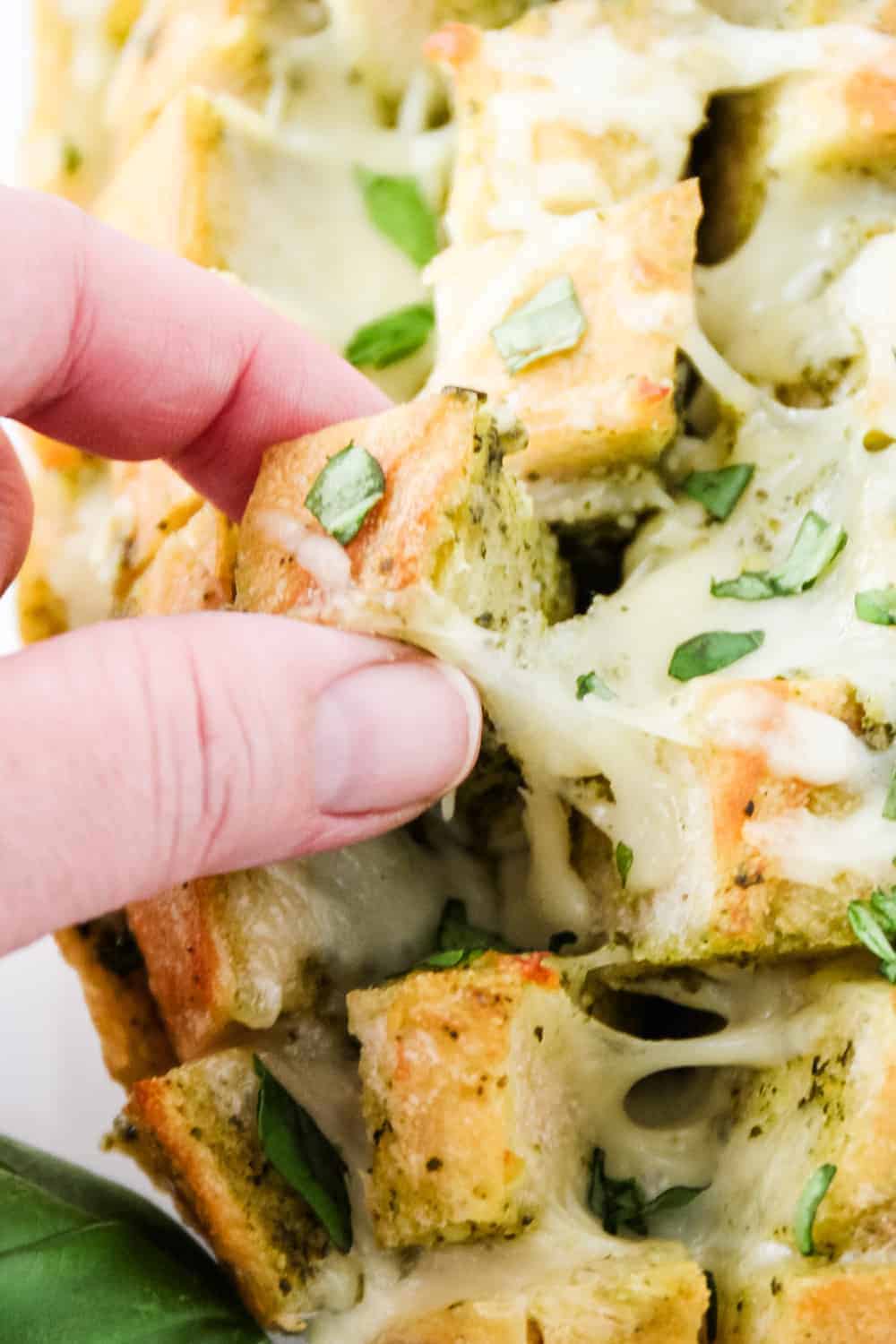 Pulling out a piece of cheesy pesto bread with finger. 