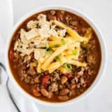 chili in a white bowl with tortilla chips and cheese