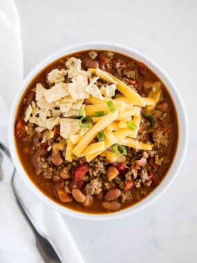 Hearty 3-ingredient chili with ground beef and beans topped with cheese and tortilla chips.