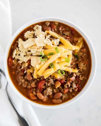 chili in a white bowl with tortilla chips and cheese