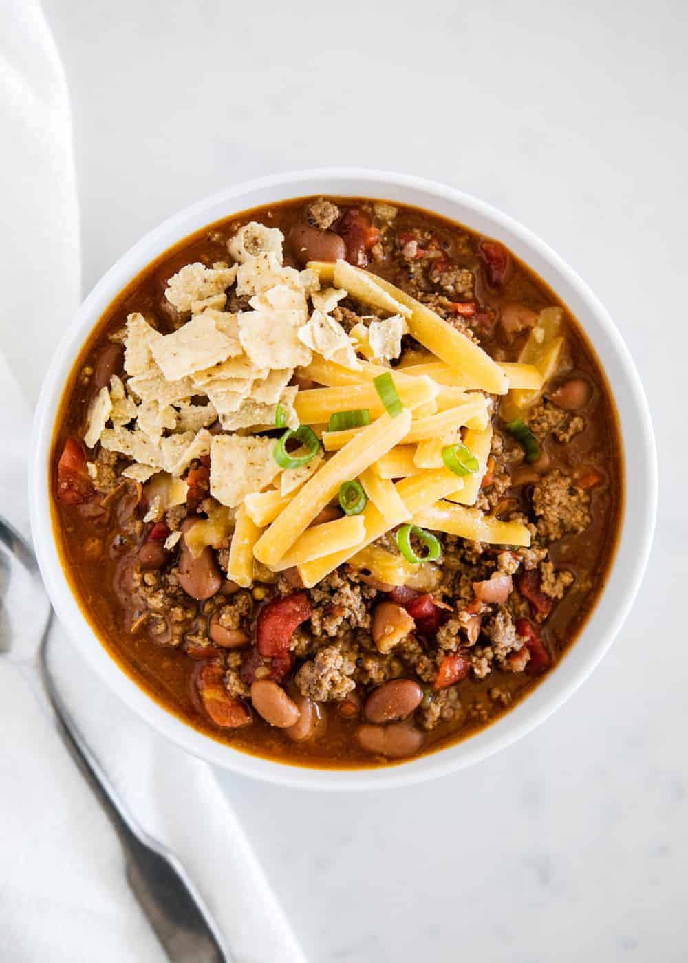 Chili in a white bowl with tortilla chips and cheese.