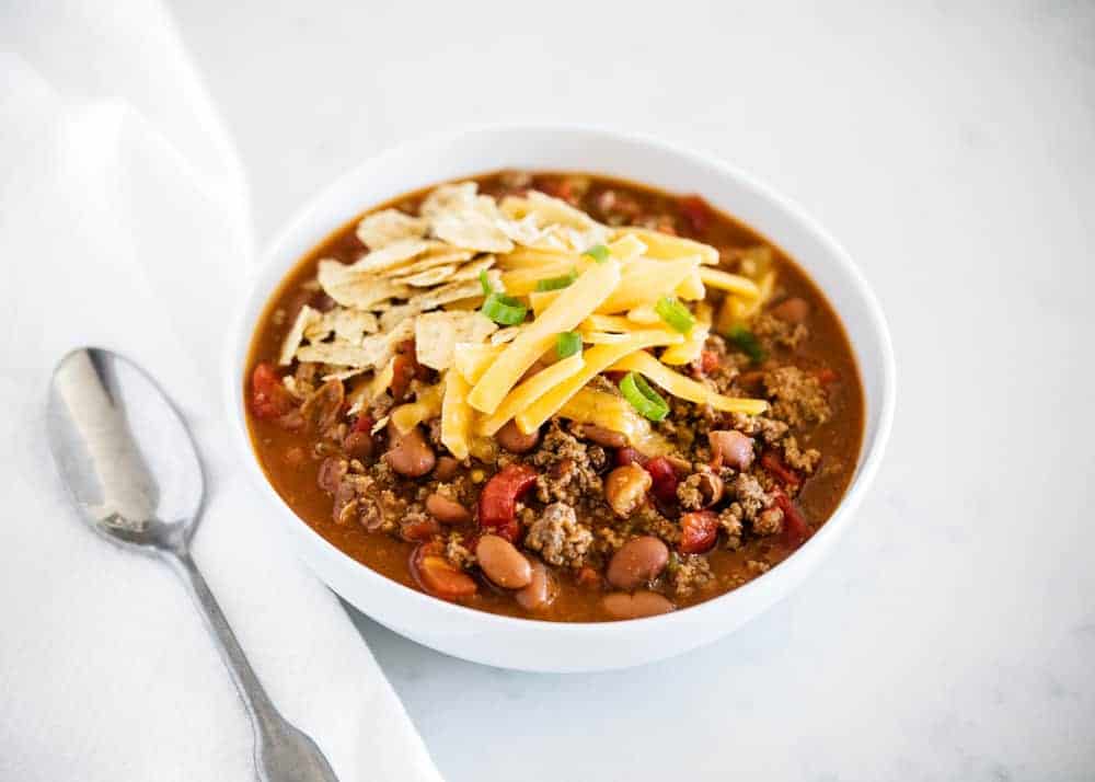 bowl of chili topped with cheese, crushed tortilla chips and green onions 