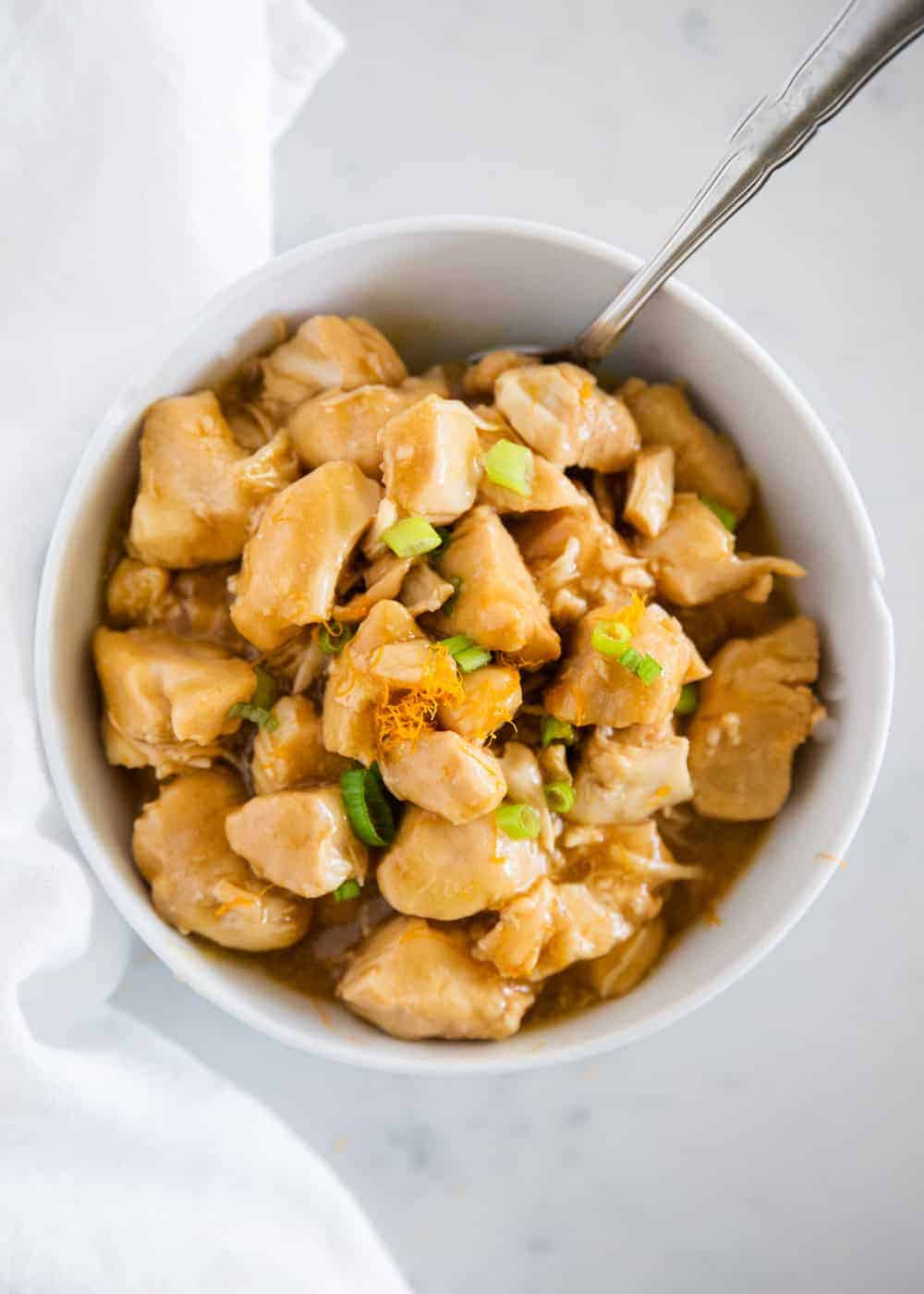 Orange chicken with green onions in white bowl.