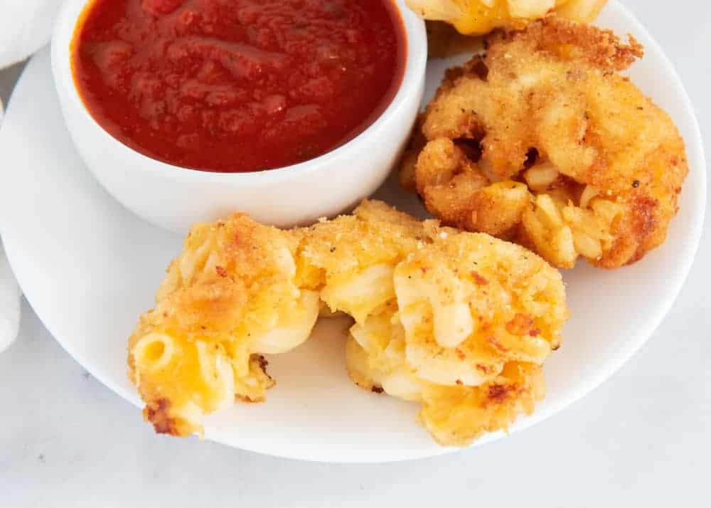 Fried mac and cheese balls on a plate with a bowl of marinara sauce.