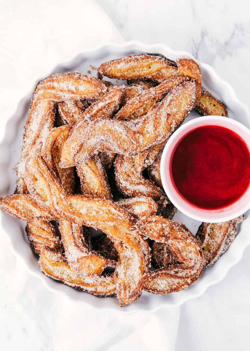 Homemade churros with raspberry sauce on white plate.