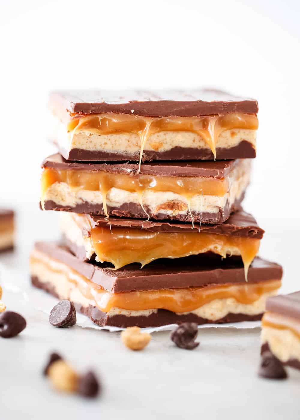Stack of homemade snickers with chocolate chips and peanuts scattered on the counter.
