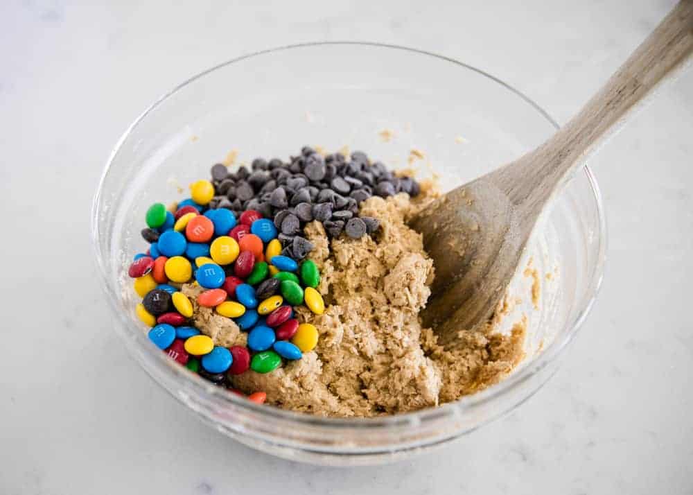 Mixing monster cookie dough in glass bowl with wooden spoon.